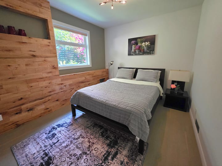 Este dormitorio principal de tamaño generoso cuenta con techos altos que hacen que la habitación se sienta abierta y espaciosa, y una gran ventana que enmarca una hermosa vista al jardín vivo justo afuera. La cama tamaño queen le ofrece todo el espacio que necesita para descansar y recargar energías.