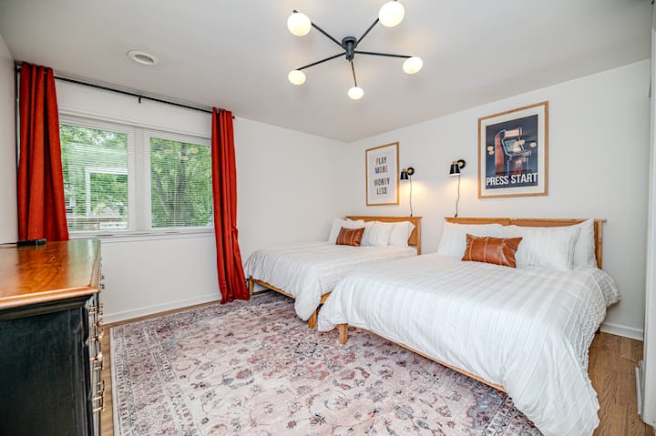 Comfortable bedroom featuring two double beds, stylish overhead lighting, and soft neutral-toned carpeting over hardwood flooring. A solid wood dresser provides ample storage space for clothing and personal belongings.