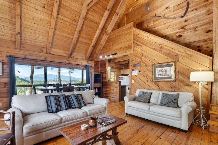 Salon chaleureux dans le chalet, avec un divan-lit taille queen, des accents en bois rustique et de grandes fenêtres offrant une vue paisible sur les montagnes.