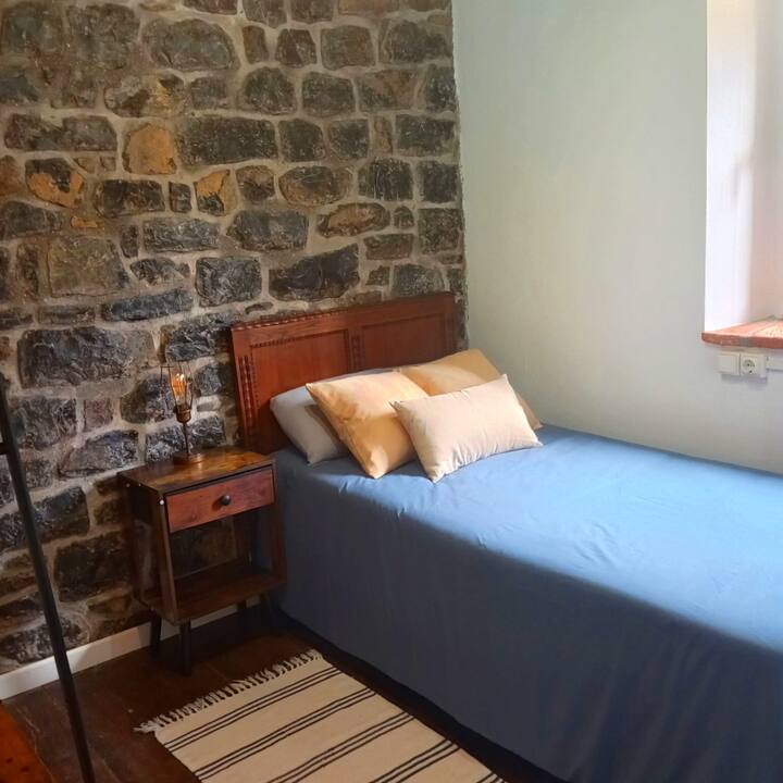 Detalle del dormitorio 2: mesilla rústica y ventana a la naturaleza.