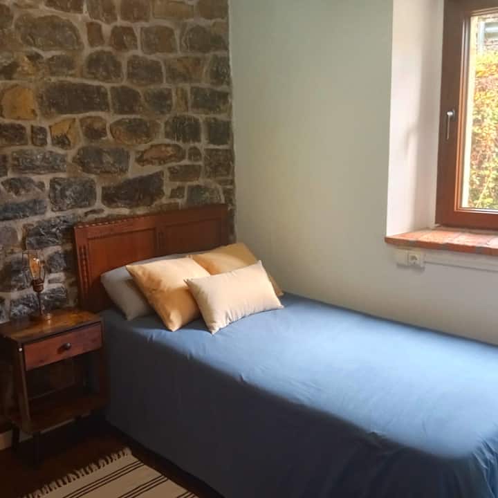 Dormitorio 2 con cabecero de madera y muro de piedra original.