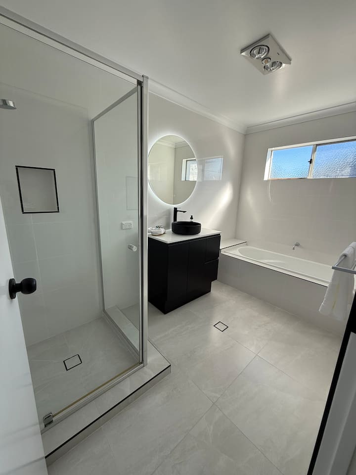Main bathroom with a bathtub, separate glass shower and vanity with a round mirror
