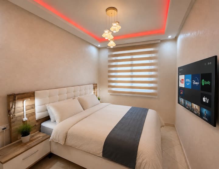 Recámara 1 por DHAJIA Morocco, diseñada como un tranquilo espacio principal para dormir con una cama tamaño king, ropa de cama estilo hotel, iluminación cálida junto a la cama, persianas para privacidad y un televisor inteligente montado en la pared listo para que los huéspedes inicien sesión en sus servicios de streaming.