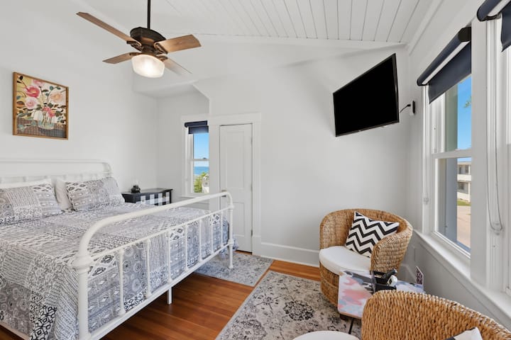 Wake up to natural light and glimpses of the water in this bright second-floor suite, complete with a comfortable bed, smart TV, and cozy seating area.