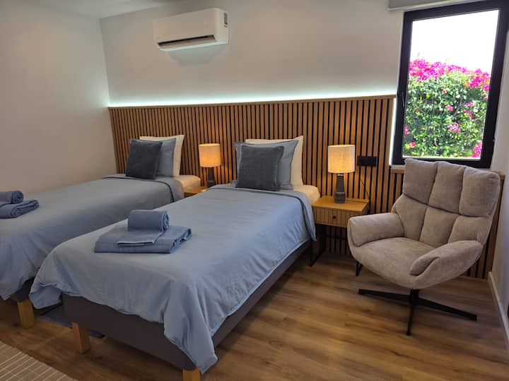 Dormitorio con dos camas individuales (90x200), una cómoda silla, aire acondicionado y un armario. Nota: Las camas individuales se pueden configurar como cama doble tamaño king, incluido un colchón completo (solicítelo antes de la llegada).