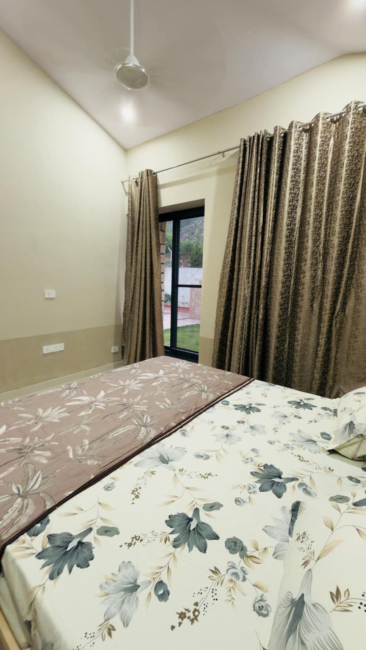 Une chambre confortable avec de la literie à fleurs, des rideaux élégants et une grande fenêtre donnant sur le jardin. Les intérieurs doux et chaleureux créent un espace paisible et confortable pour se détendre.