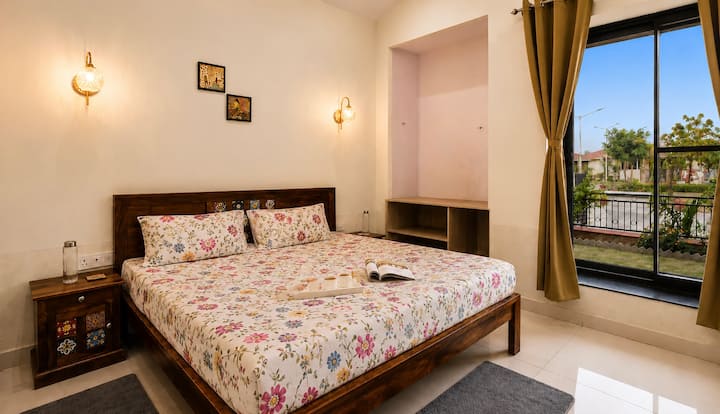 Une chambre lumineuse et chaleureuse avec un lit double confortable, des meubles en bois élégants, un éclairage chaleureux et une grande fenêtre offrant une vue agréable et beaucoup de lumière naturelle.