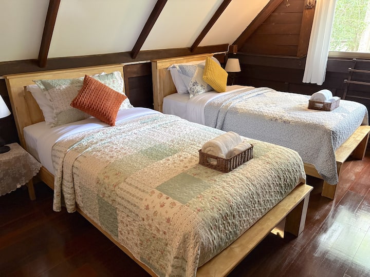 Conçu pour accueillir confortablement les familles et les petits groupes, le loft supérieur dispose de trois lits dans un espace ouvert. Les hauts plafonds en bois, les poutres apparentes et les grandes fenêtres allient confort, caractère et charme rustique.