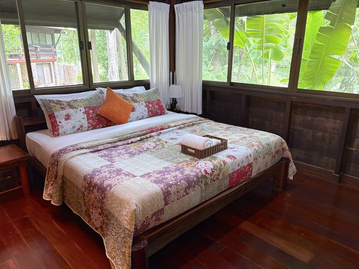 Réveillez-vous en pleine nature dans cette chambre principale confortable. Les plafonds hauts, les riches détails en bois et les grandes fenêtres créent un espace lumineux et relaxant avec de belles vues sur la forêt à l'extérieur.