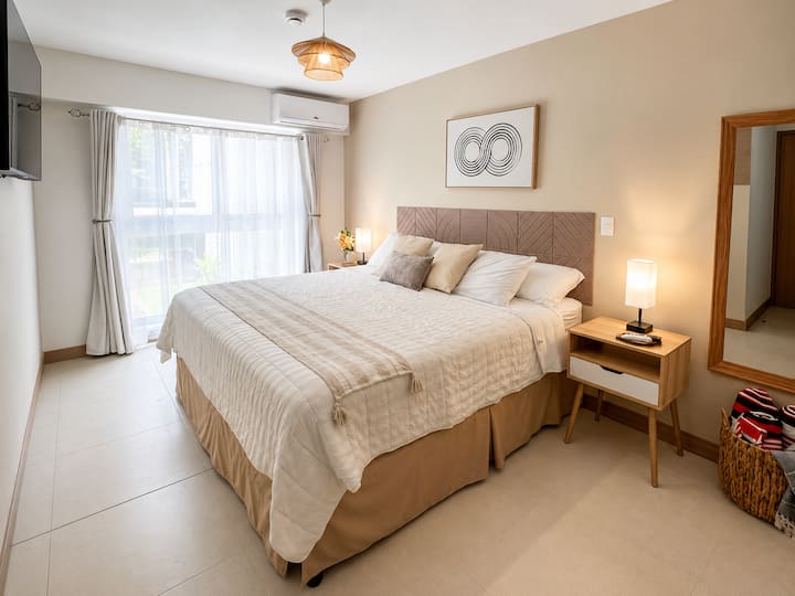 Habitación principal con una cómoda cama King rodeada de tonos cálidos y detalles cuidadosamente seleccionados para crear una experiencia acogedora y elegante. Además con un TV de 50in para ver tu serie favorita.