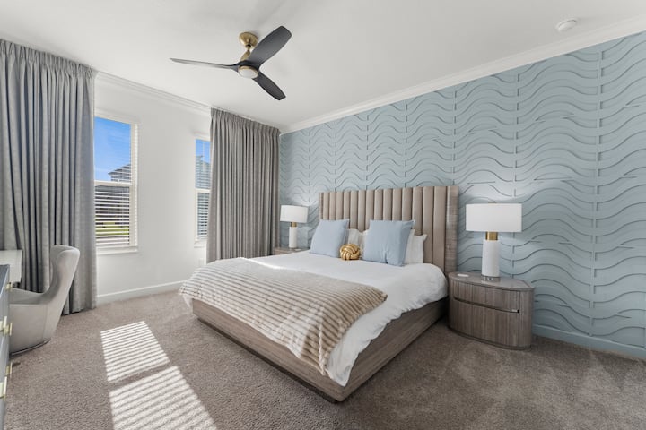Duerme hasta tarde en la cama tamaño king mientras la luz de la mañana inunda la habitación. Cabecera acolchada, ventilador de techo y cortinas opacas: tu propio refugio tranquilo.