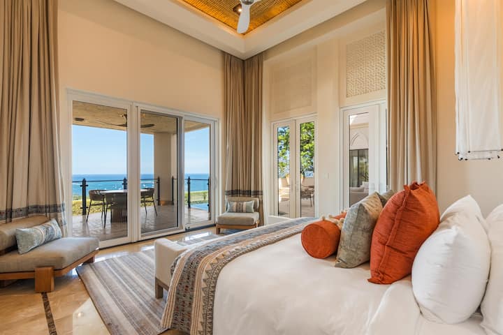 Bedroom — bed close-up, terracotta/orange pillows,  motorized sheers, ocean