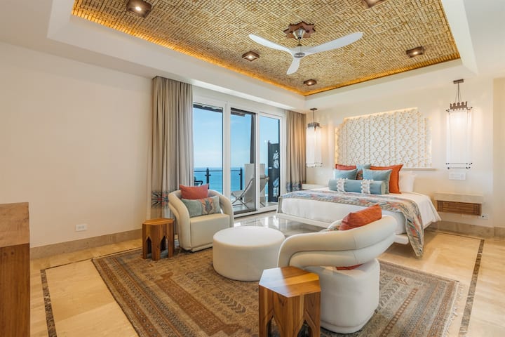 Bedroom — pendant chandeliers, white pod armchairs, gold mosaic ceiling, ocean view