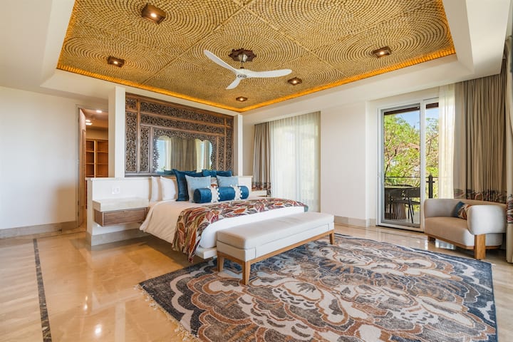 Upper Floor Master Bedroom — dark carved headboard, antiqued mirror, concentric circle stone ceiling, blue/floral bedspread, terrace view
