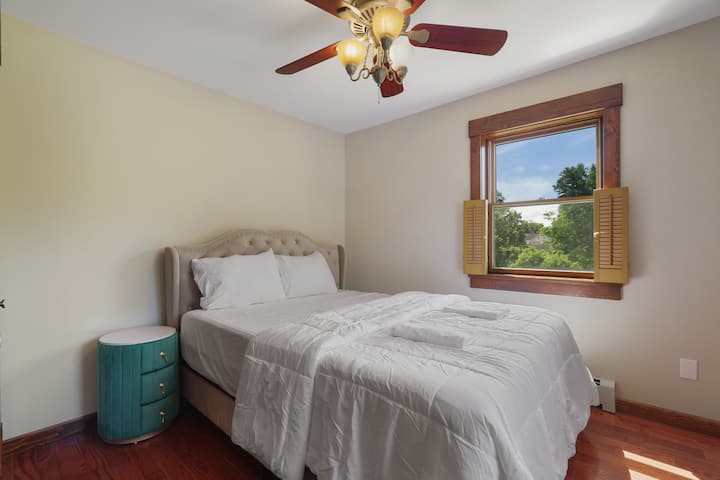 cama queen com colchão de espuma, mesa de cabeceira e persianas de madeira nas janelas com vista para a propriedade