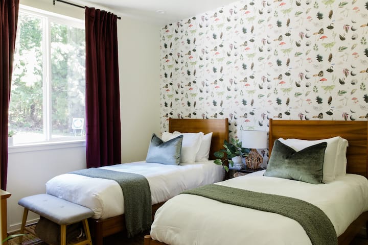 Dieses einladende Schlafzimmer mit zwei Einzelbetten verfügt über eine von der Natur inspirierte Tapete, weiche Bettwäsche und warme Holzakzente, die einen komfortablen Rückzugsort für Kinder, Freund:innen oder zusätzliche Gäste schaffen.