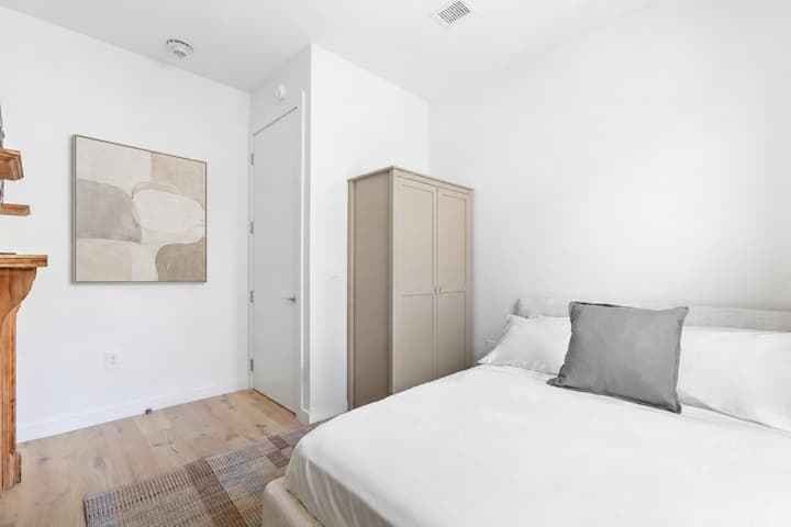 Large primary bedroom has a queen sized bed, decorative fireplace, hanging wardrobe, and luggage rack. Black-out roller shades on windows.