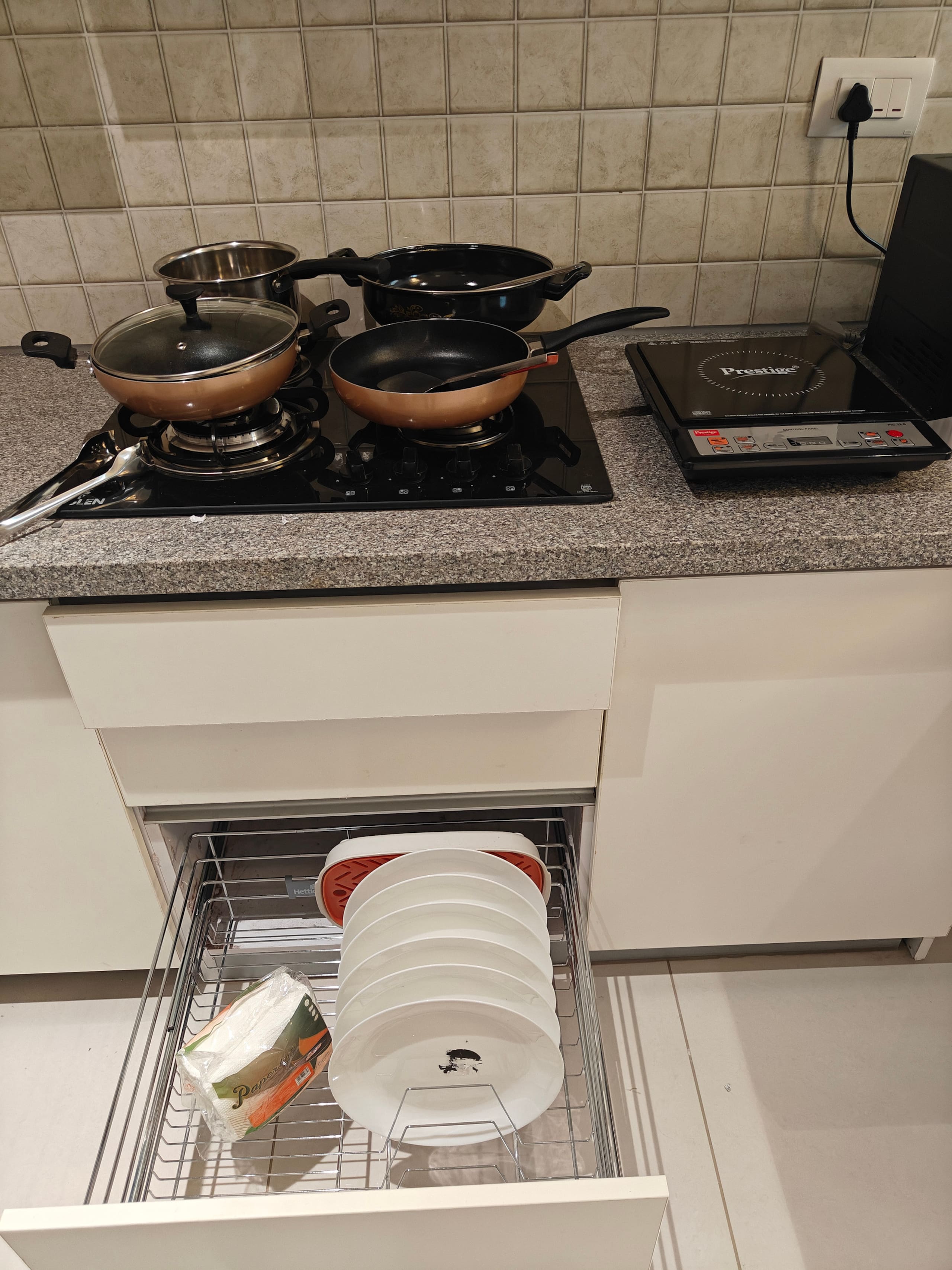 Cookware on the hob above a drawer of plates