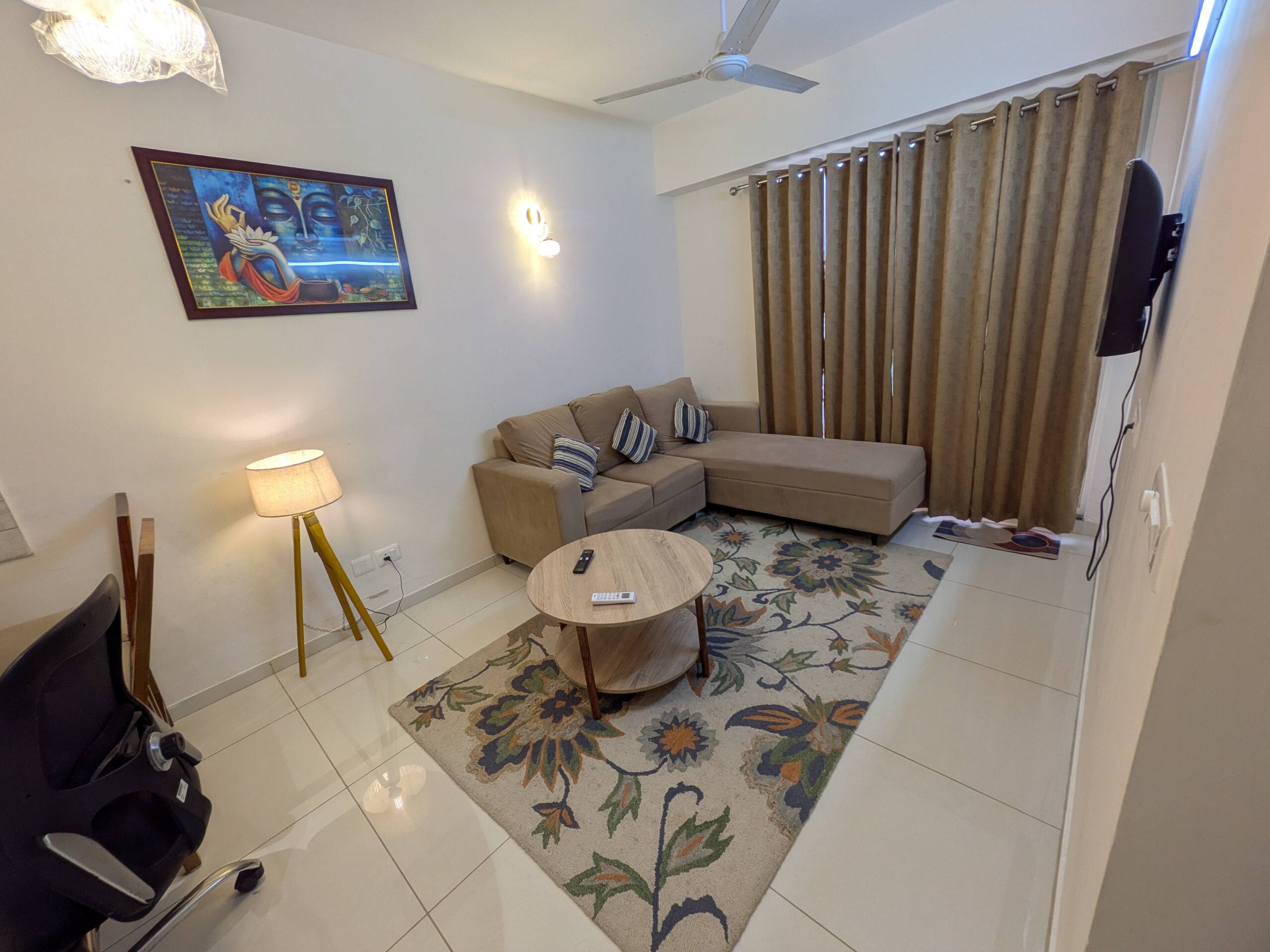 Living room with L-shaped sofa, floral rug, round wooden coffee table, tripod floor lamp and colourful artwork