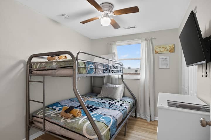 Acogedora habitación con literas con ropa de cama divertida, luz natural, ventilador de techo y un televisor montado en la pared para huéspedes adicionales.