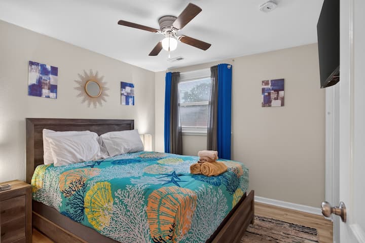 Acogedora habitación costera con colorida ropa de cama inspirada en el mar, detalles en azul, ventilador de techo y una cama cómoda para una estadía relajante.