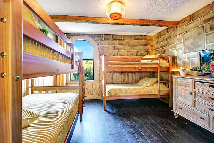 Two sets of sturdy wooden bunks facing each other across honeyed stone walls, golden afternoon light streaming through the arch. Perfect for the kids who want to stay up whispering all night.