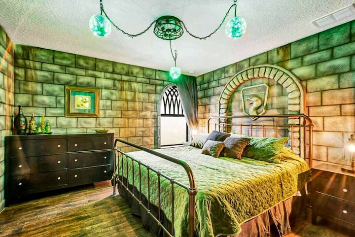 Green dungeon light, stone walls, a serpent crest glowing above the iron-frame bed — the Emerald Serpent Suite runs deeper than the others. Slytherin always does.