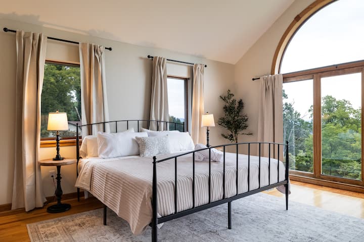 Light-filled bedroom with arched windows and peaceful treetop views