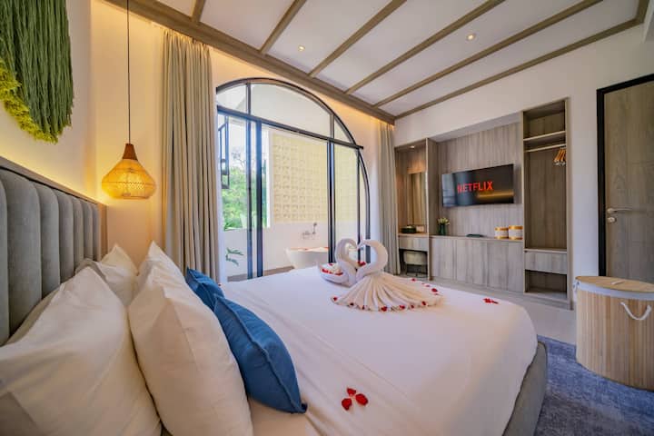 Recámara 1 con ventana de arco, ropa de cama azul y blanca y cálidas luces colgantes.