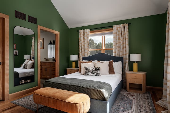 Queen bedroom with rich green walls, layered bedding, and peaceful views of the surrounding property.