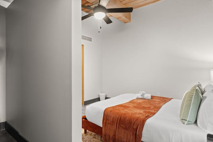 Spálňa s veľkou manželskou posteľou, teplým textilom a priemyselným stropným ventilátorom