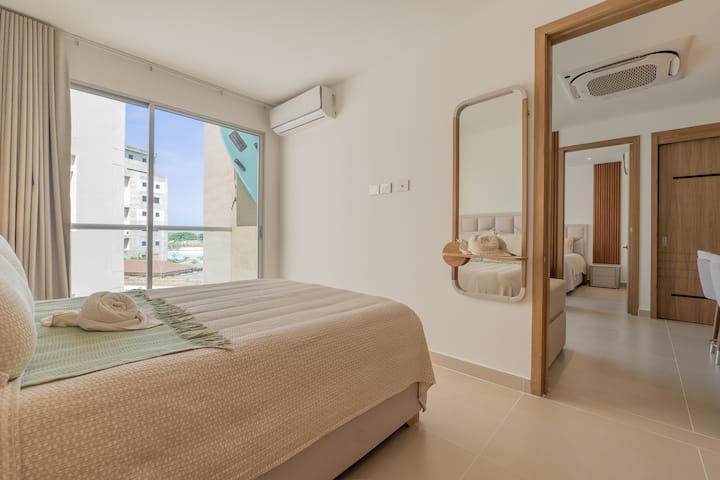Habitación luminosa y acogedora con cama confortable, aire acondicionado, amplias ventanas y acabados en madera que brindan un ambiente moderno y fresco para descansar.
