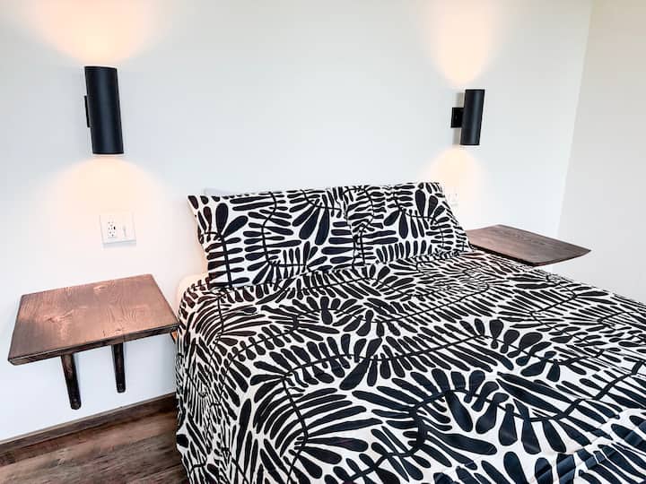 The guest bedrooms offer comfortable queen memory foam beds and a wall of windows (not shown). Each person has their own custom-designed floating white-oak side table, reading light, and USB/USB-C power adapters to charge all of their devices.