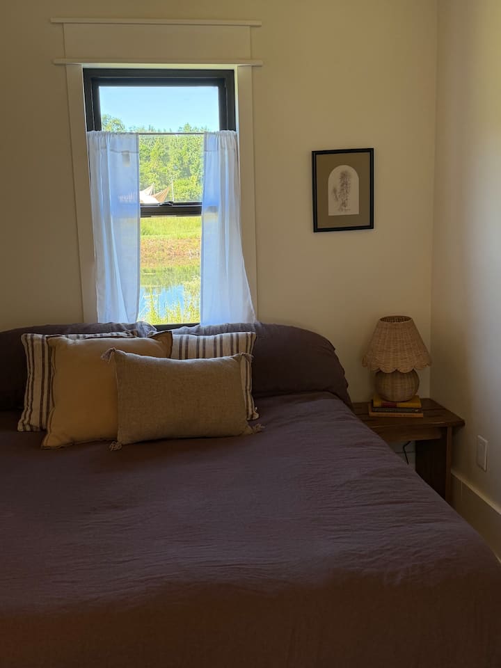 The cottage bedroom with a linen-covered bed and a view of the pond through the window