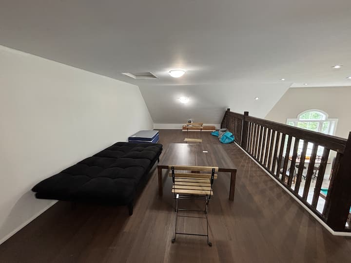 Chambre 6 · Ce deuxième angle du loft montre le futon, la table basse et la balustrade ouverte. Le plafond mesure environ six pieds de haut et l'espace de couchage donne sur la salle de jeux en dessous.