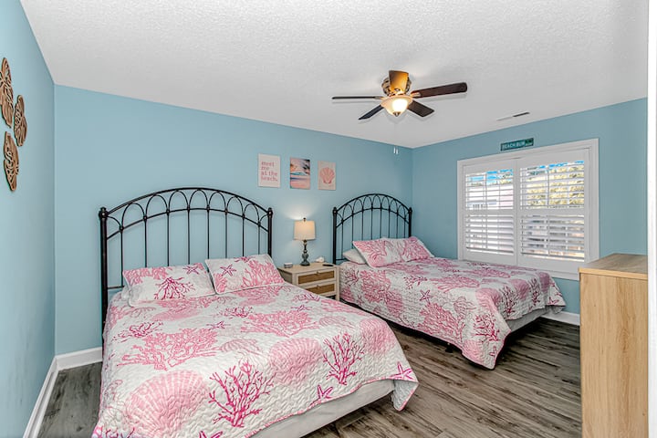 Bright coastal bedroom with two beds, beach decor, and sunny shutters