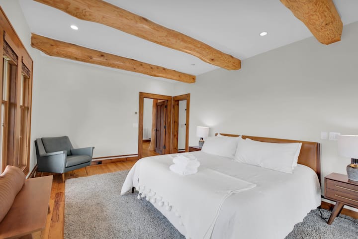 The primary suite has its own dressing area beyond the double mirrored doors, folded towels waiting on linens beneath rustic beams.
