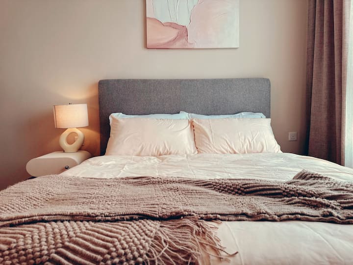 Boutique-style luxury meets wabi-sabi calm. Features a padded grey headboard, custom ceramic lamp base, textured wall art, and premium bedding for an elevated rest experience.