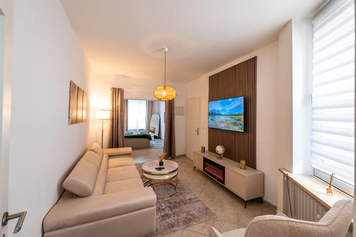 Sala de estar luminosa y acogedora con un cómodo sofá, un televisor inteligente grande y una chimenea eléctrica decorativa, perfecta para relajarse y descansar después de un largo día.