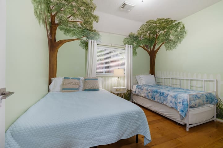 Habitación para niños con mural de árbol, cama matrimonial y sofá cama individual