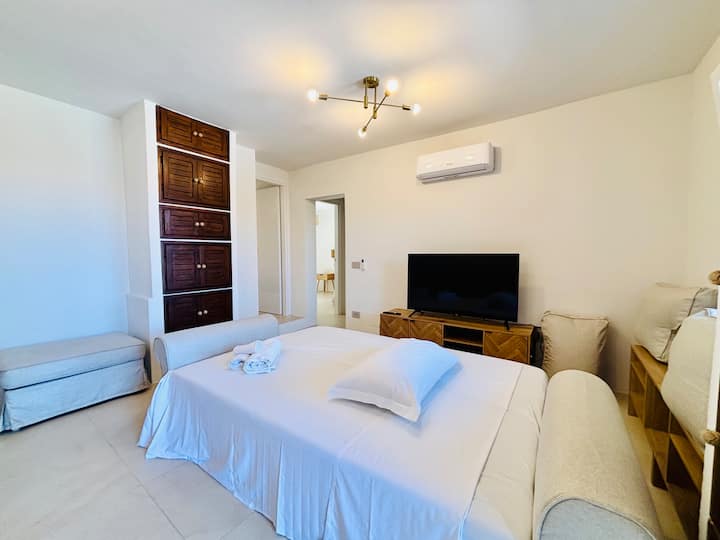 Sala de estar con sofá cama convertible en cama, televisor inteligente de alta definición y aire acondicionado. Las puertas al fondo conducen a la zona de dormitorios con tres habitaciones dobles y dos baños.