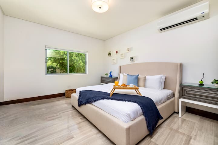 Dormitorio luminoso y acogedor con una cómoda cama tamaño king, muebles elegantes, sábanas suaves y una tranquila vista al jardín. Un refugio relajante con mucha luz natural. La habitación también ofrece la comodidad de un baño privado en suite.