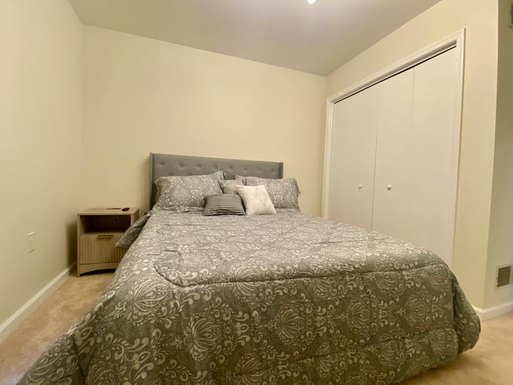 This bedroom is located on the main level. It has a queen bed, dresser, nightstand, full-length mirror, and a Smart TV.