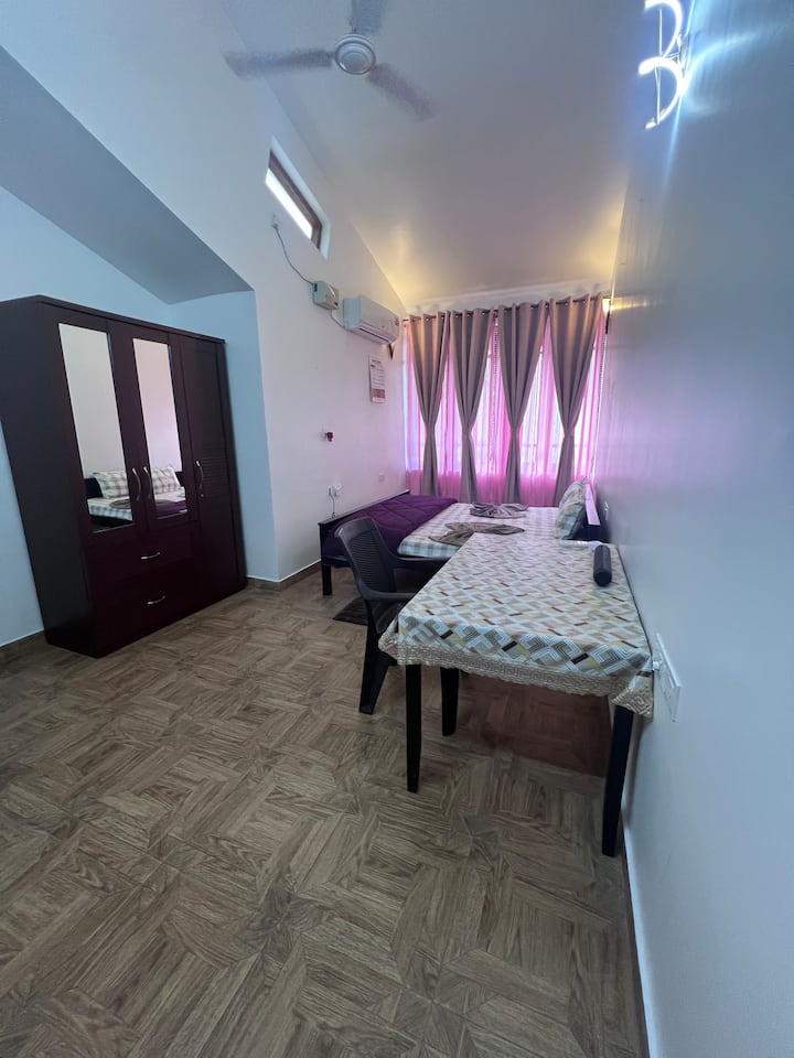 a Spacious Master bedroom Includes a Queen Bed, a study table, an Almirah, AC and a bluetooth speaker.
