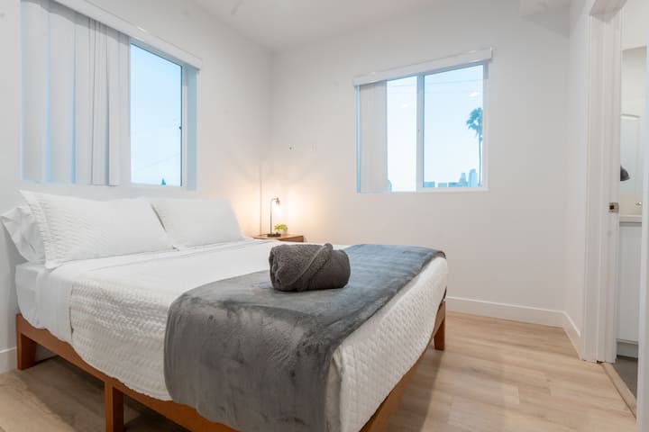 Une chambre confortable avec un grand lit, de grandes fenêtres, la climatisation centralisée, une table de chevet et une lampe pratique.