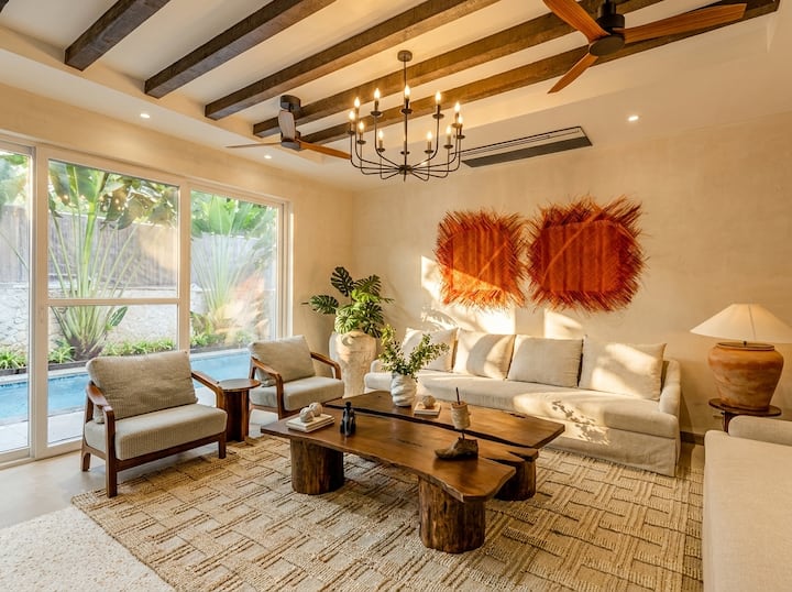 Living room opens straight onto the pool deck. Exposed beams, lime-plaster walls, and light that does most of the work. Seating for the full group without anyone perching on an arm.