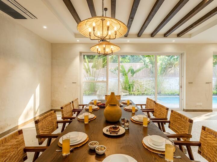 Dining room looking toward the pool. Long teak table, woven chairs, and enough room to spread out a card game after dinner.