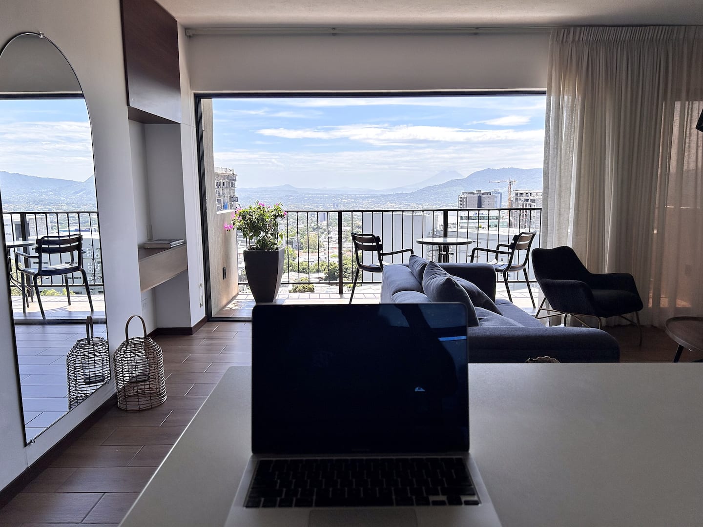Sala amplia con sofá gris y balcón abierto con vista a la ciudad