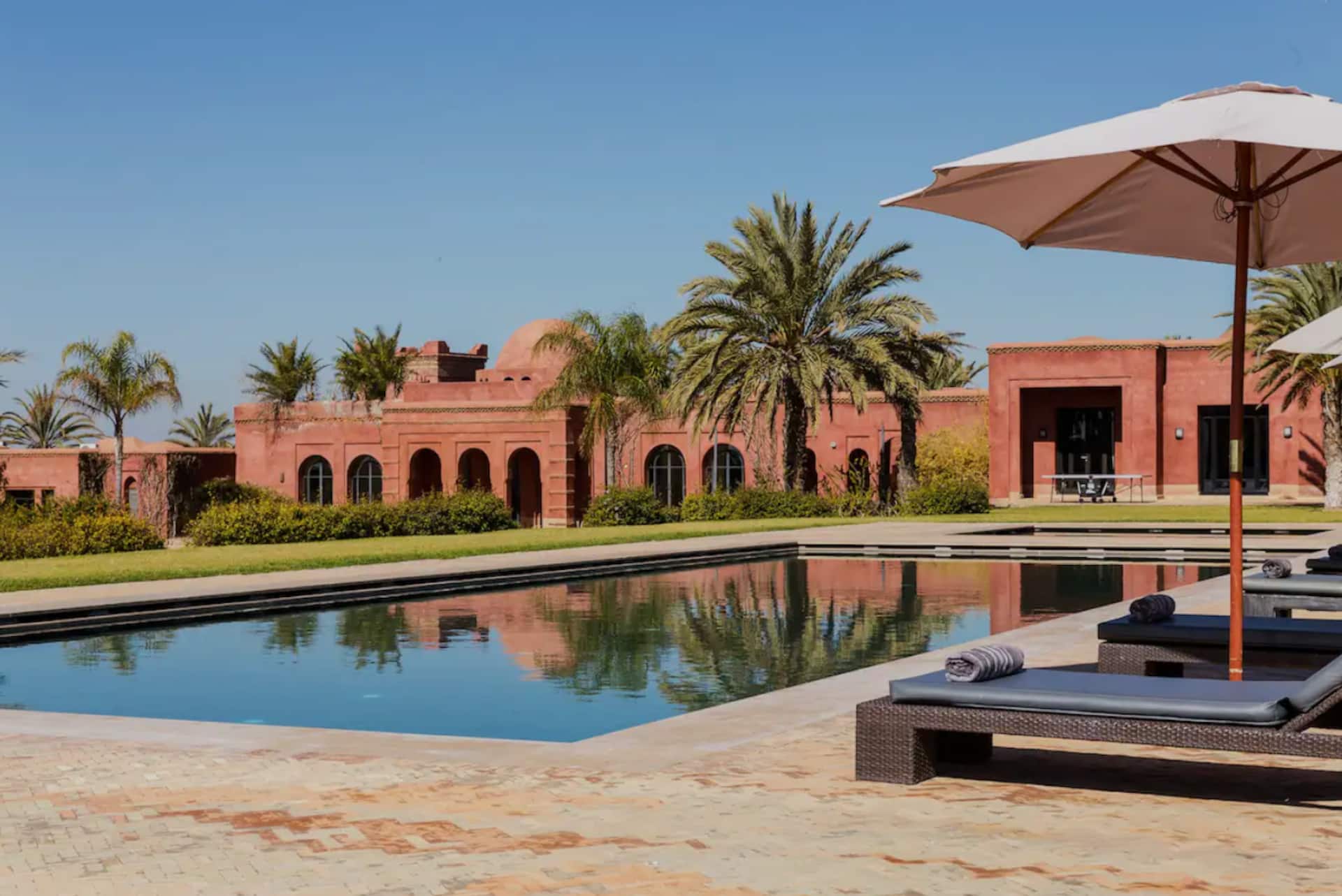 Villa Tameslohte's terracotta façade and palm trees reflected in the 20 × 7 m pool, beside shaded loungers