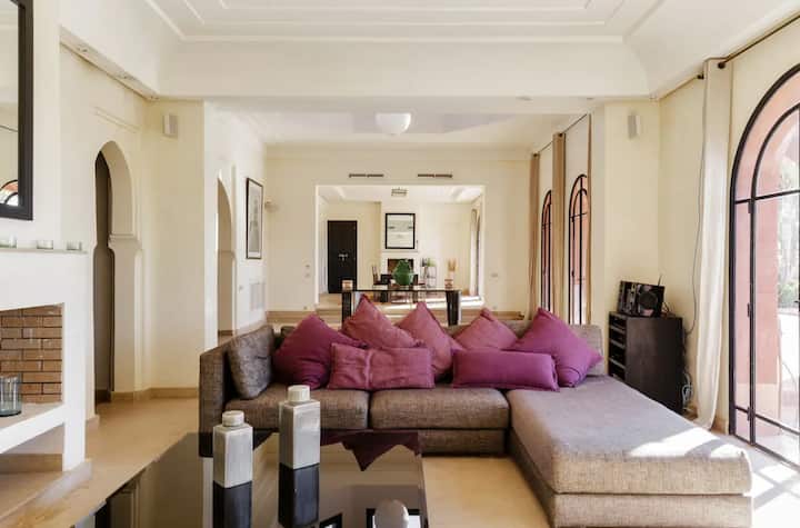Reception room at Villa Tameslohte with a deep corner sofa, plum cushions and tall arched doors onto the patio